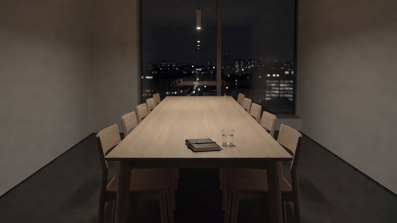 A meeting room after hours: a long oak table, chairs pushed in, a single closed notebook, a window onto a dark city